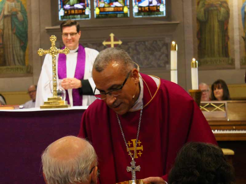 Bishop Fenty delivering communion, Father Dan smiling in the background.